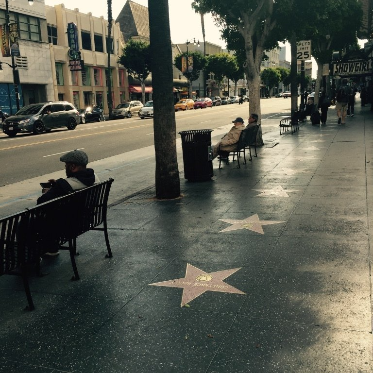 A man sits on a bench next to a star on the sidewalk