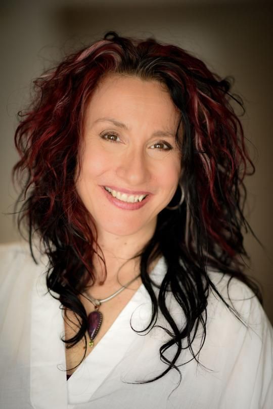 A woman with red and black hair is smiling and wearing a white shirt