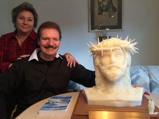 A man and woman pose with a statue of jesus wearing a crown of thorns