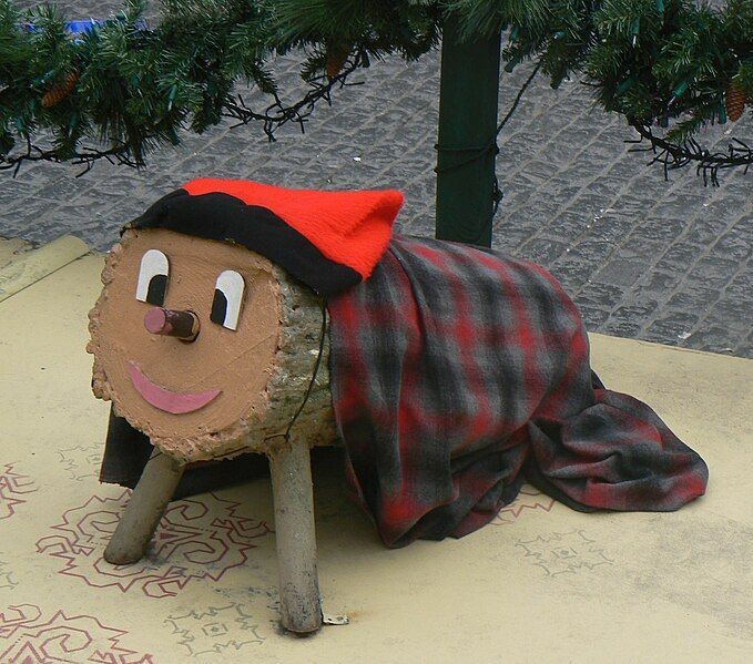 A stuffed animal is wrapped in a plaid blanket and has a red hat on