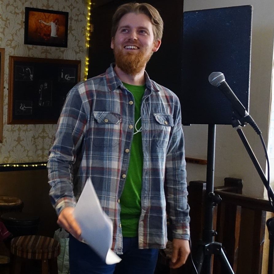 A man in a plaid shirt is holding a piece of paper in front of a microphone