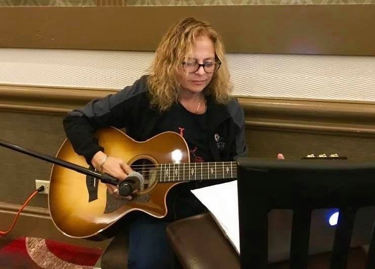 A woman is playing an acoustic guitar in front of a microphone.