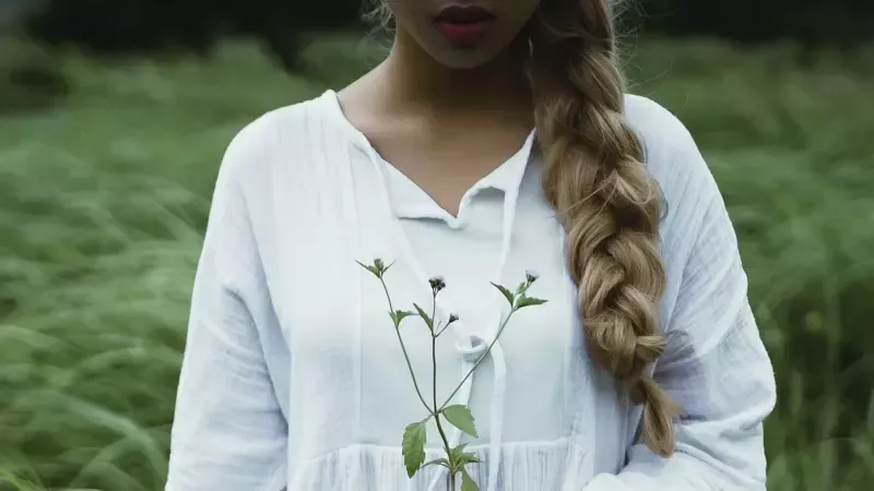 A woman in a white dress is holding a plant in her hands.