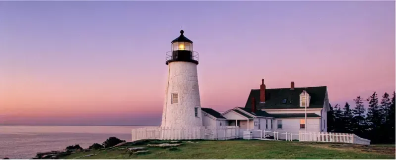 A lighthouse sits on a cliff overlooking the ocean at sunset.