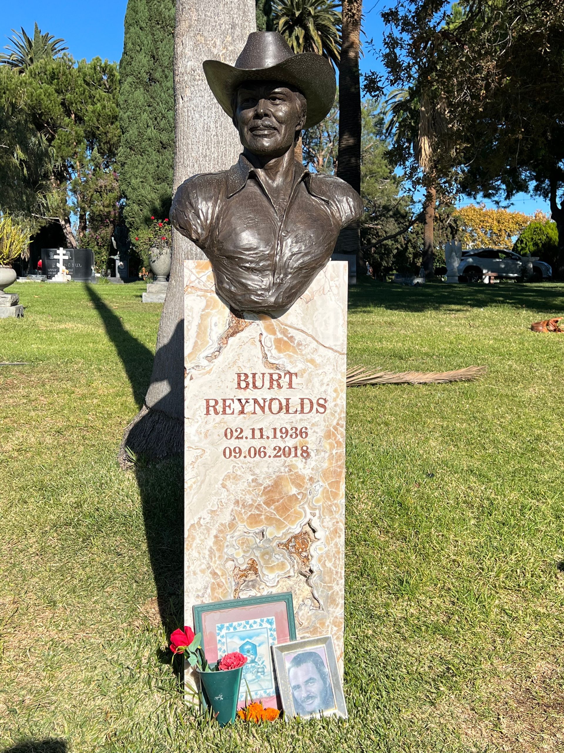 A statue of a man in a cowboy hat is on a grave in a cemetery.