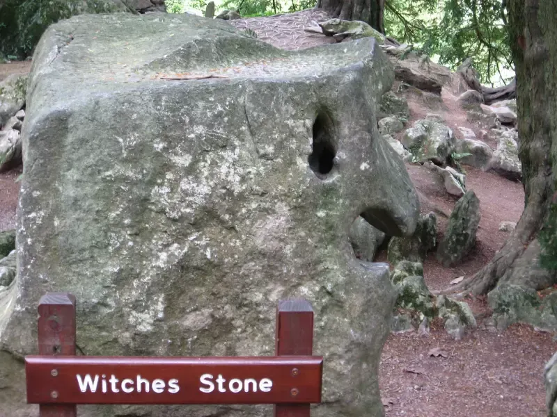 A sign that says witches stone in front of a large rock