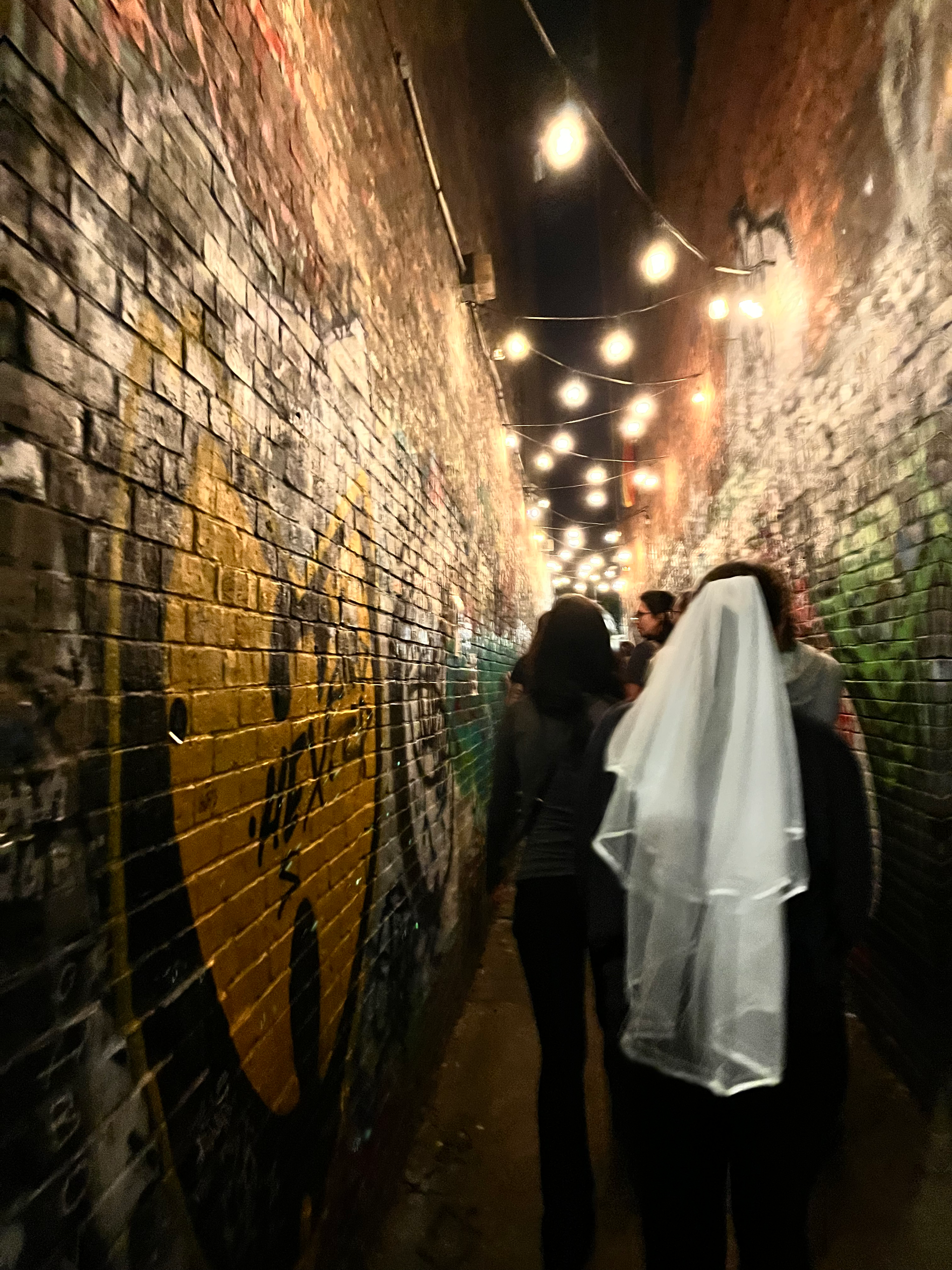 A woman in a white veil walks through a tunnel with graffiti on the wall