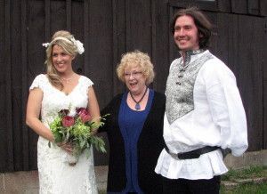 A bride and groom are posing for a picture with a woman in a blue dress.