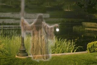 A ghost is standing next to a lamp post in a park.