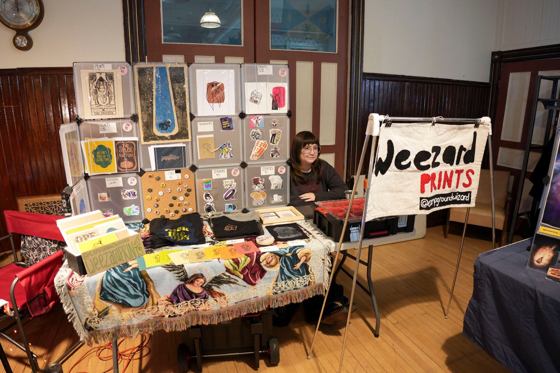 A woman sits in front of a table with a sign that says jecond prints