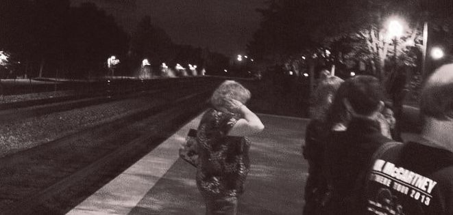 A group of people are standing on a train platform at night.