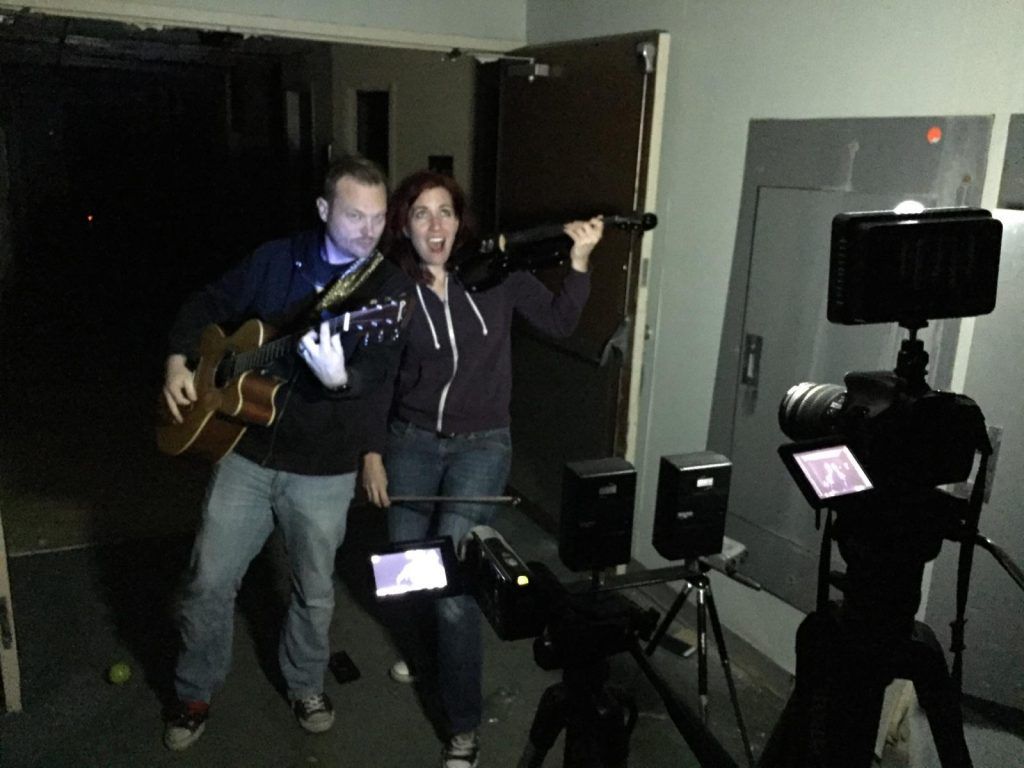 A man playing a guitar and a woman singing in front of a camera