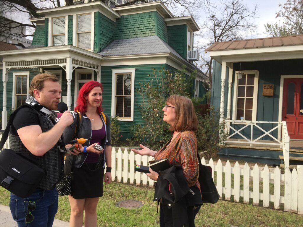 A man is talking to two women in front of a green house.