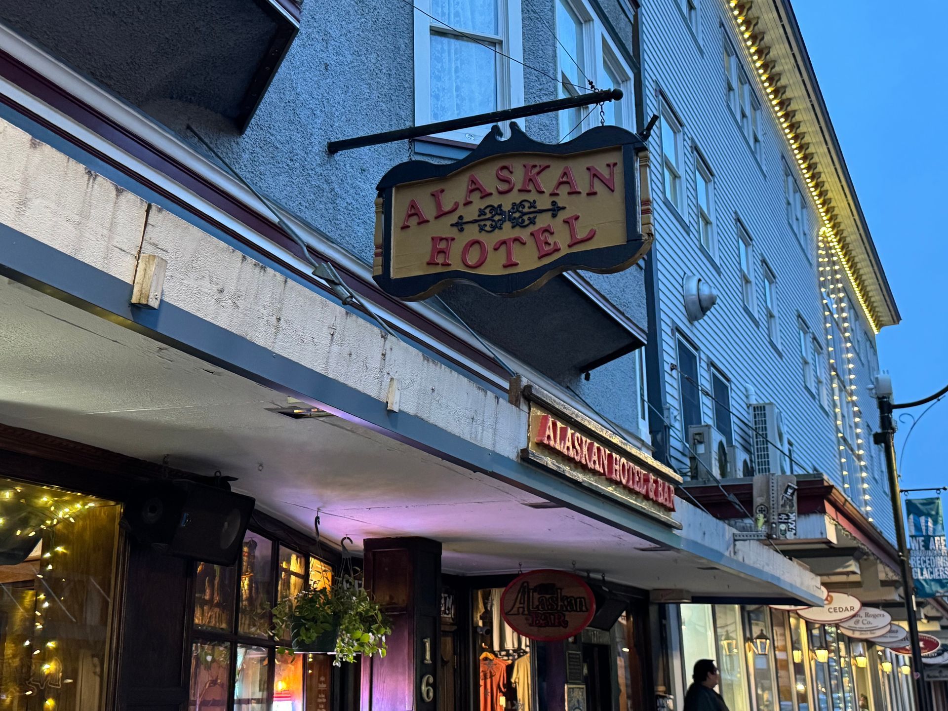 A sign for the alaskan hotel hangs from the side of a building