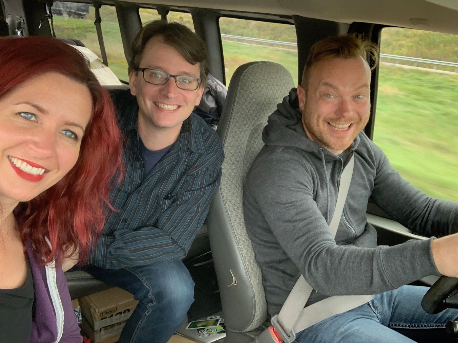 Three people are sitting in the back seat of a van and smiling.