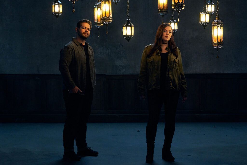 A man and a woman are standing in a dark room with lanterns hanging from the ceiling.