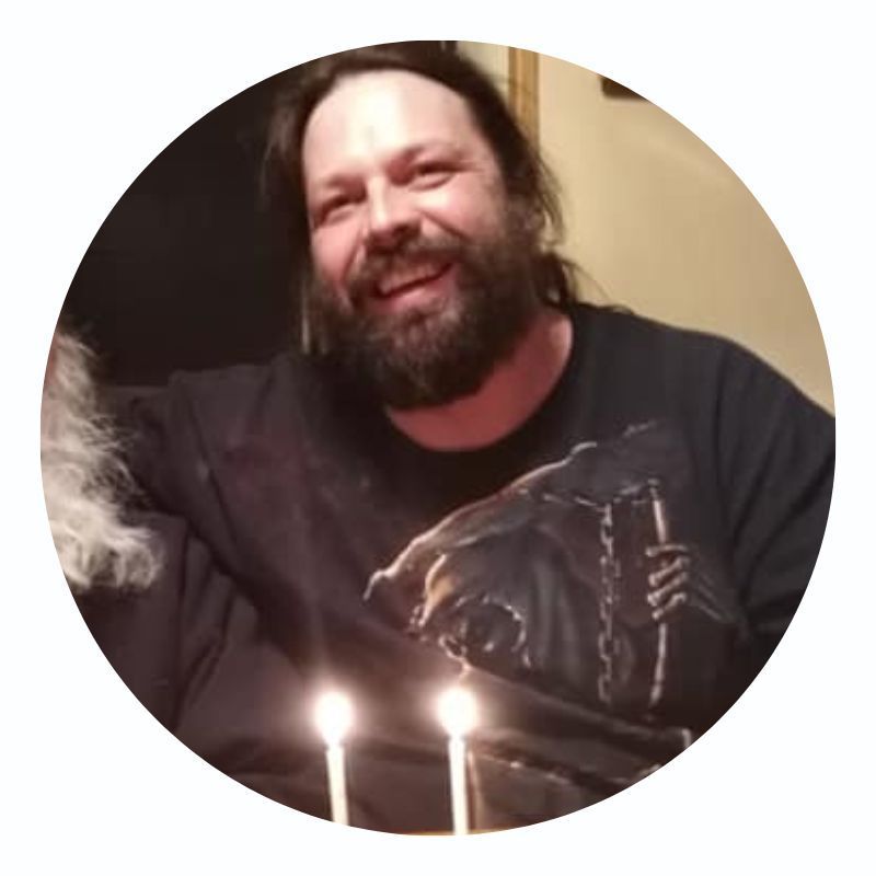 A man with a beard is smiling in front of a birthday cake