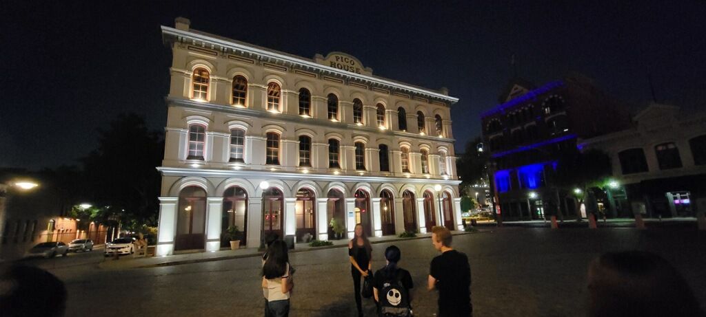 A group of people are standing in front of a large building at night.