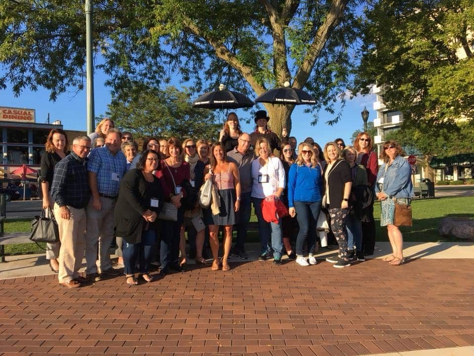 A group of people standing in front of a tree with umbrellas