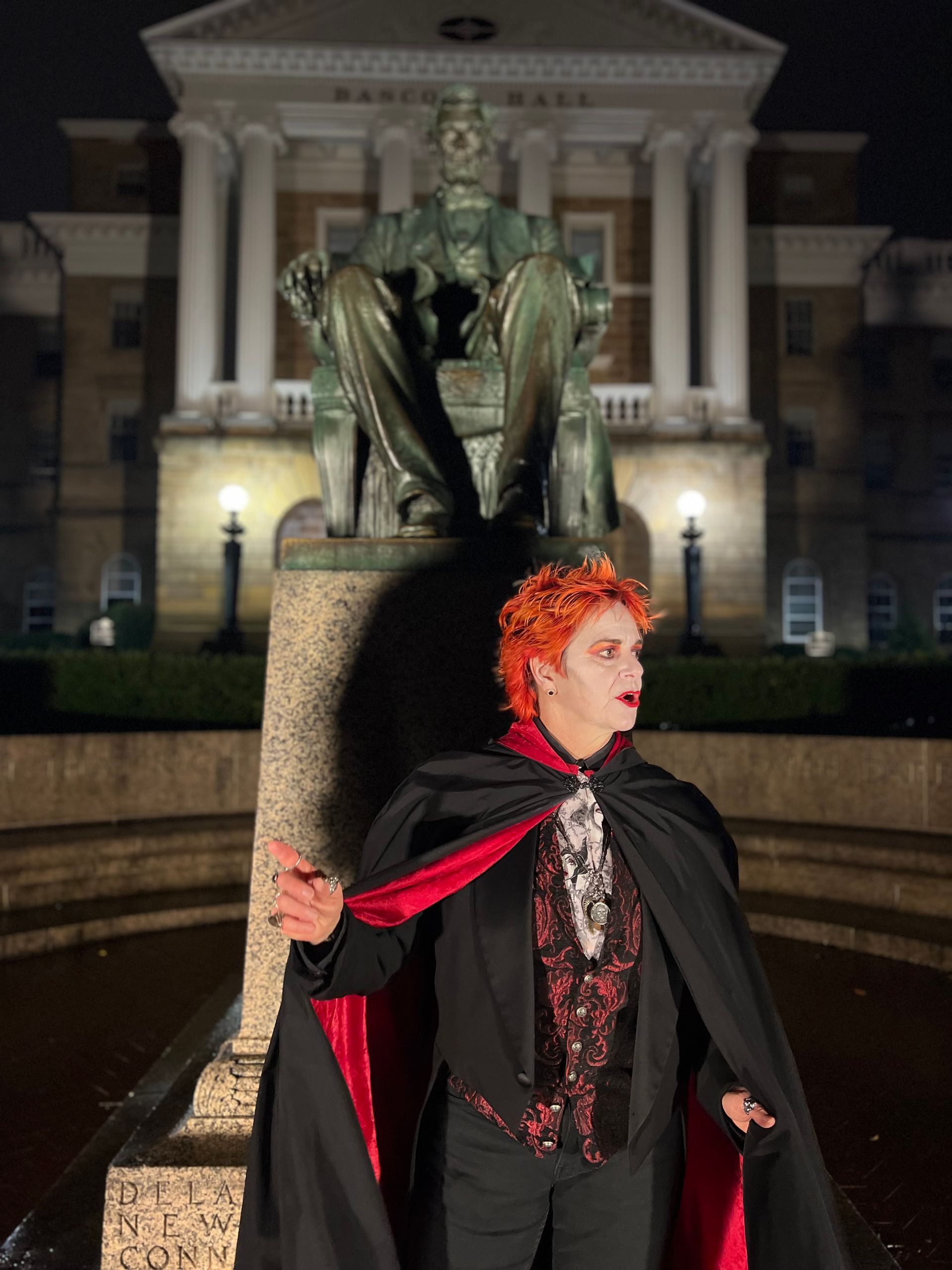 A man in a vampire costume stands in front of a statue