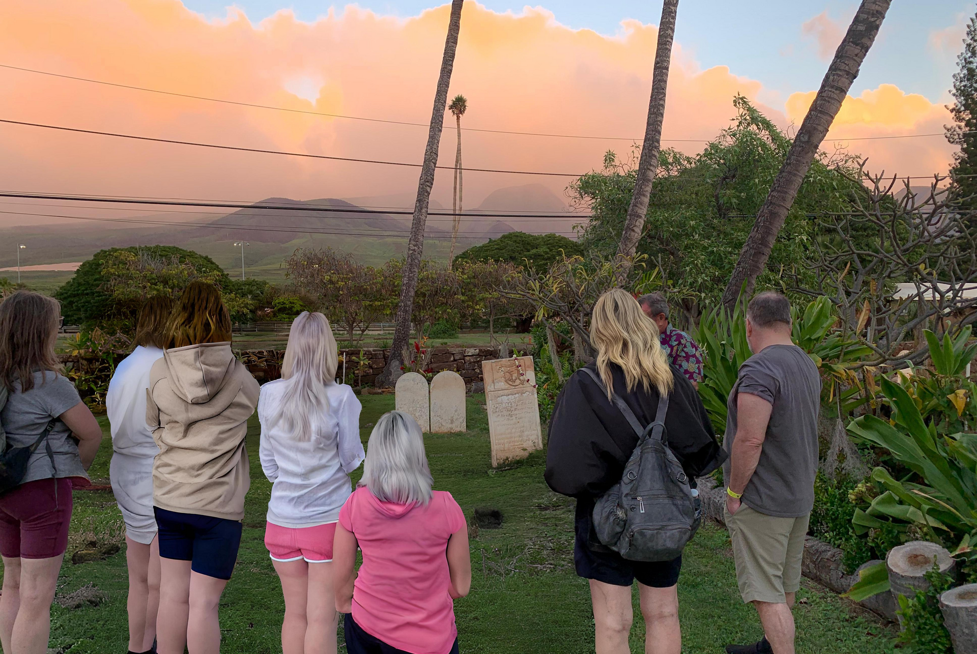 A group of people are standing in front of a cemetery at sunset.