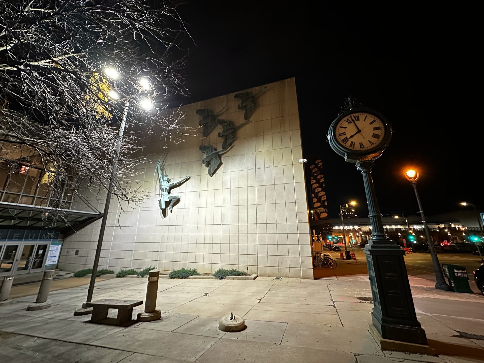 A clock stands in front of a large building at night