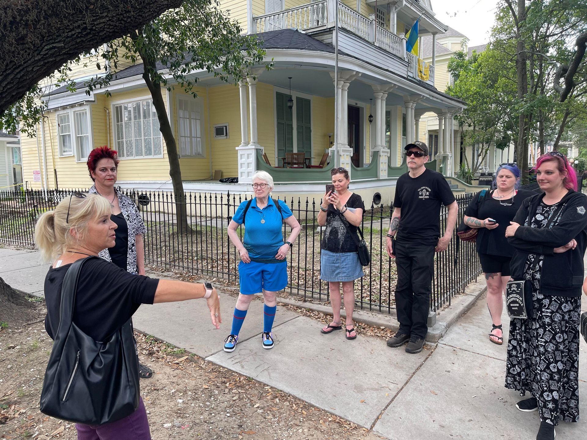 A group of people standing on a sidewalk in front of a yellow house