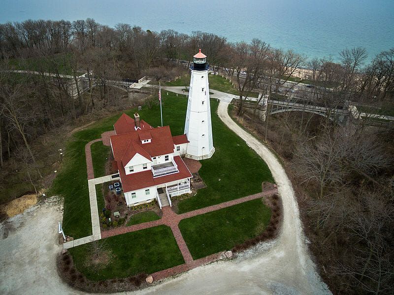 An aerial view of a lighthouse surrounded by trees and grass.