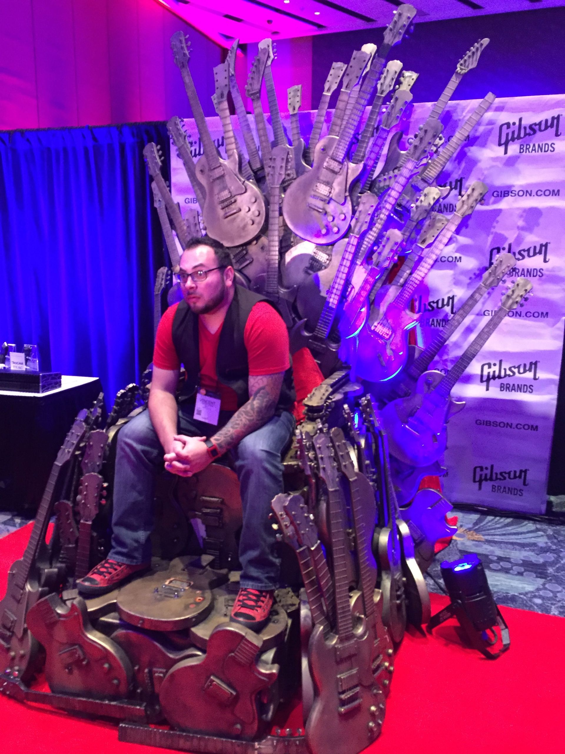 A man is sitting on a throne made out of guitars.