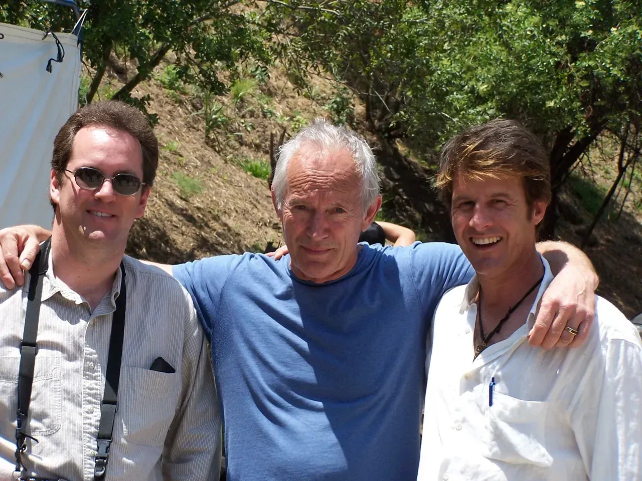 Three men posing for a picture with one wearing a camera strap