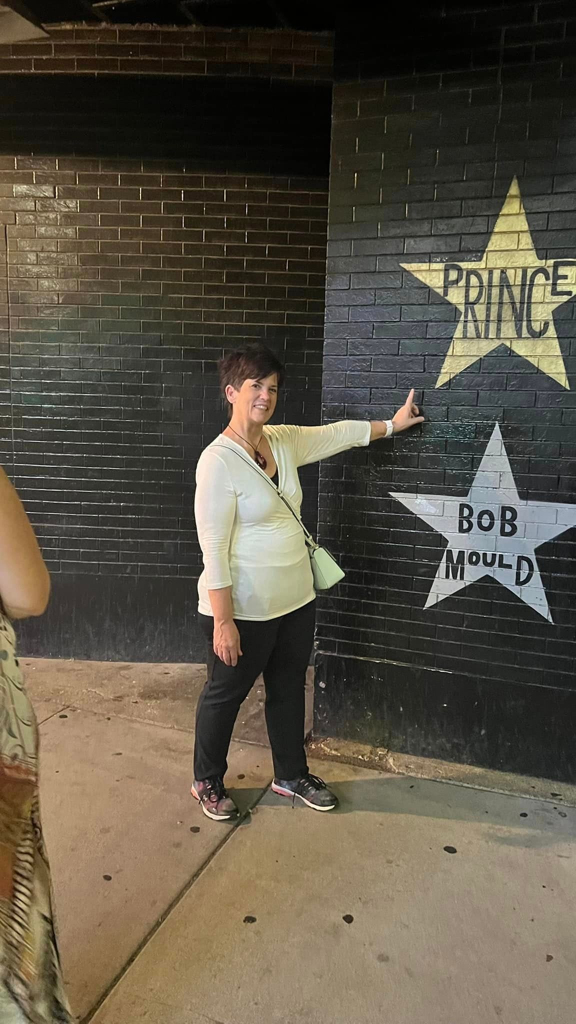 A woman is pointing at a star on a brick wall