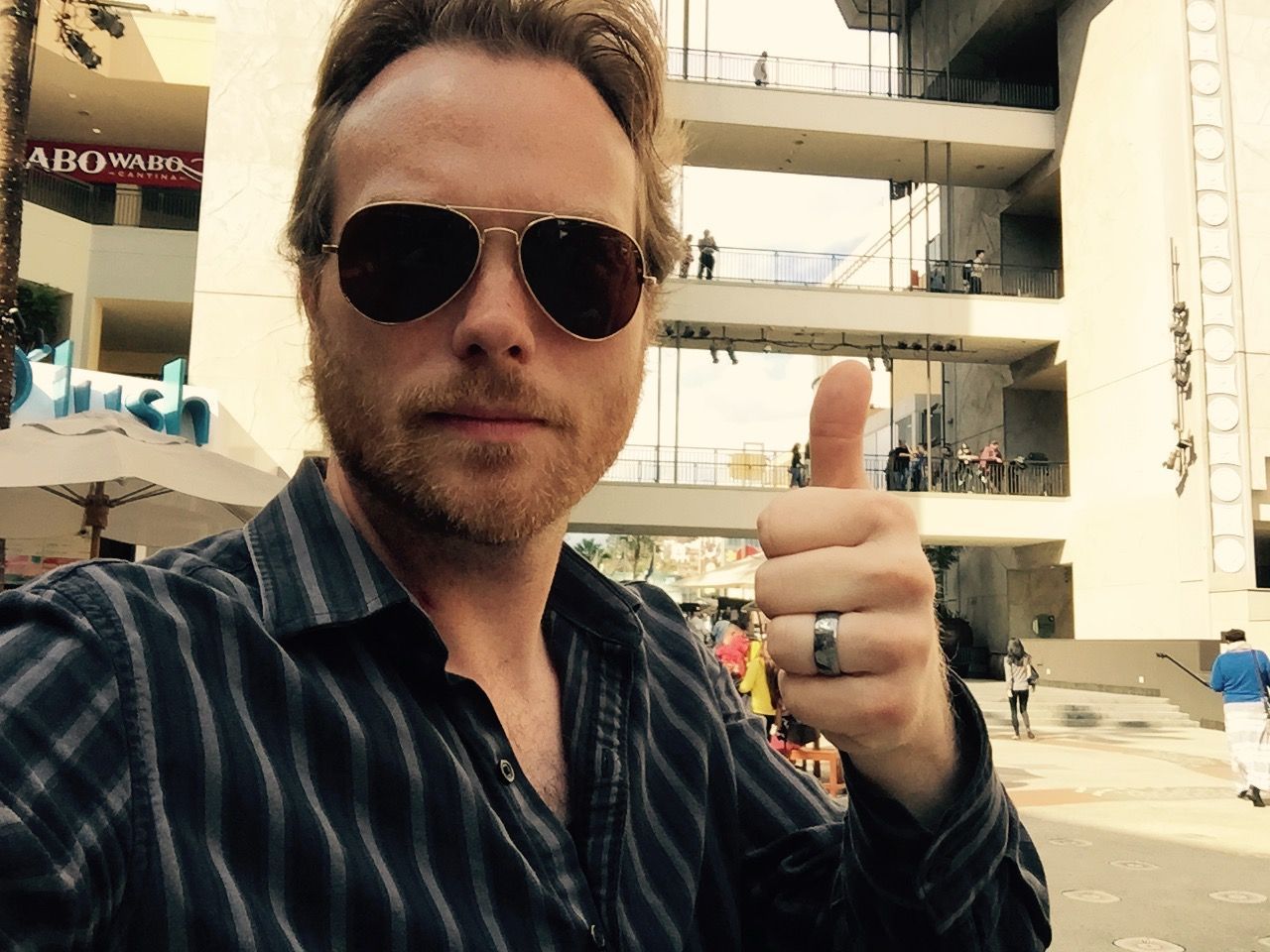 A man wearing sunglasses and a ring is giving a thumbs up