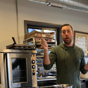 A man in a green hoodie stands in front of a stainless steel oven