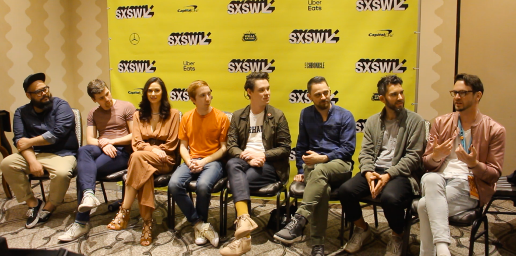 A group of people are sitting in chairs in front of a yellow wall.