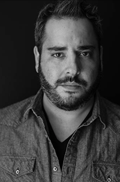 A black and white photo of a man with a beard wearing a denim shirt.