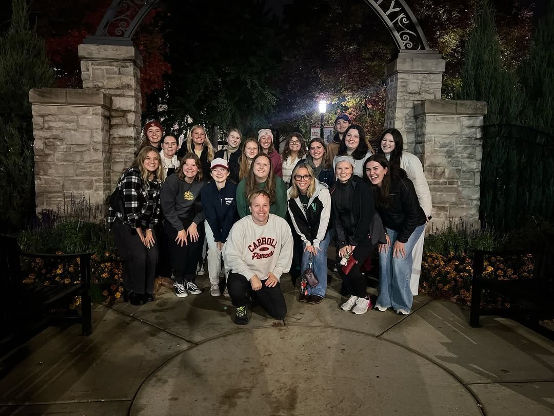 Group of people posing for photo under a stone archway at night.