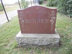 A red gravestone with the word butcher carved into it is sitting in the grass.