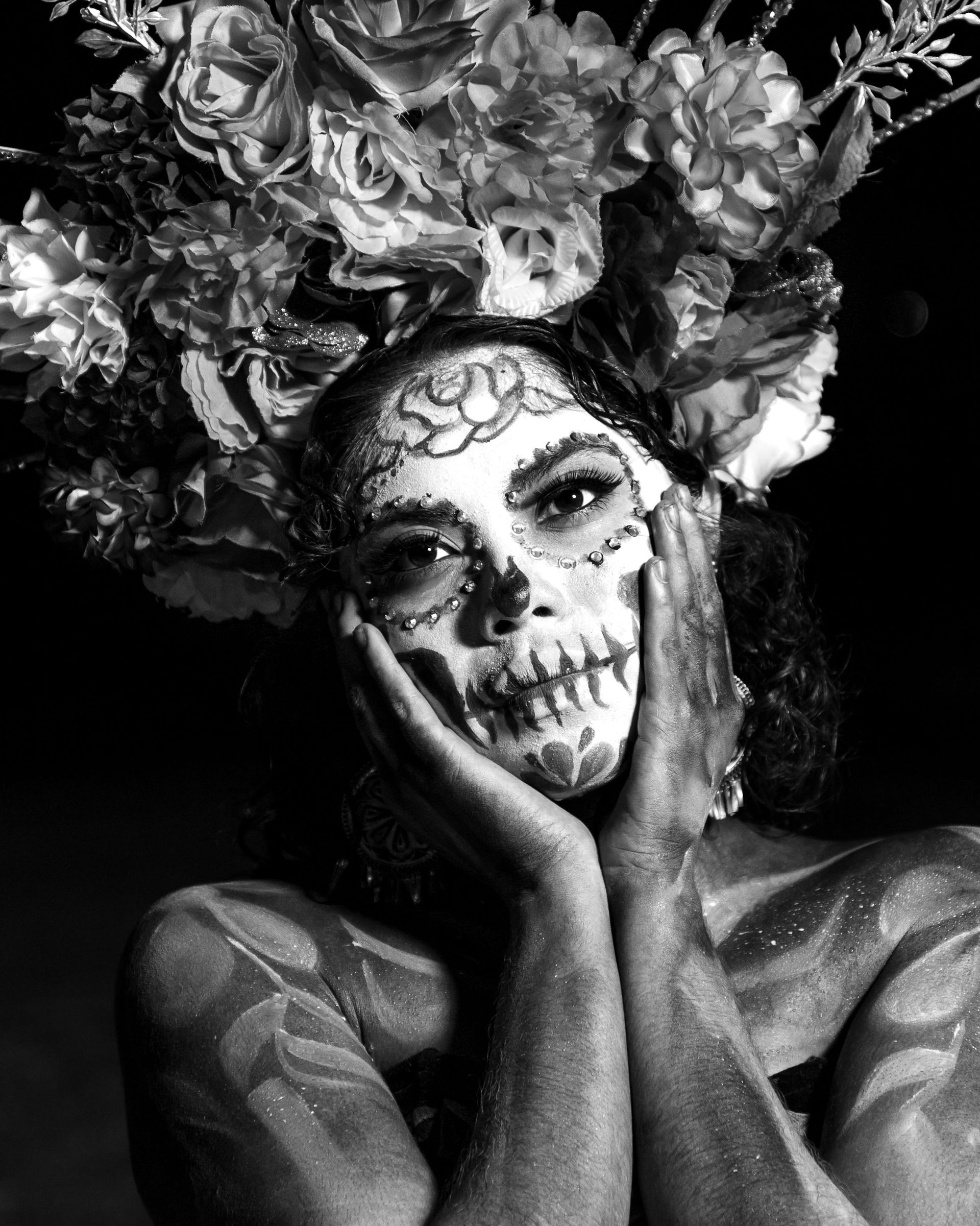 A black and white photo of a woman with sugar skull makeup and flowers in her hair.