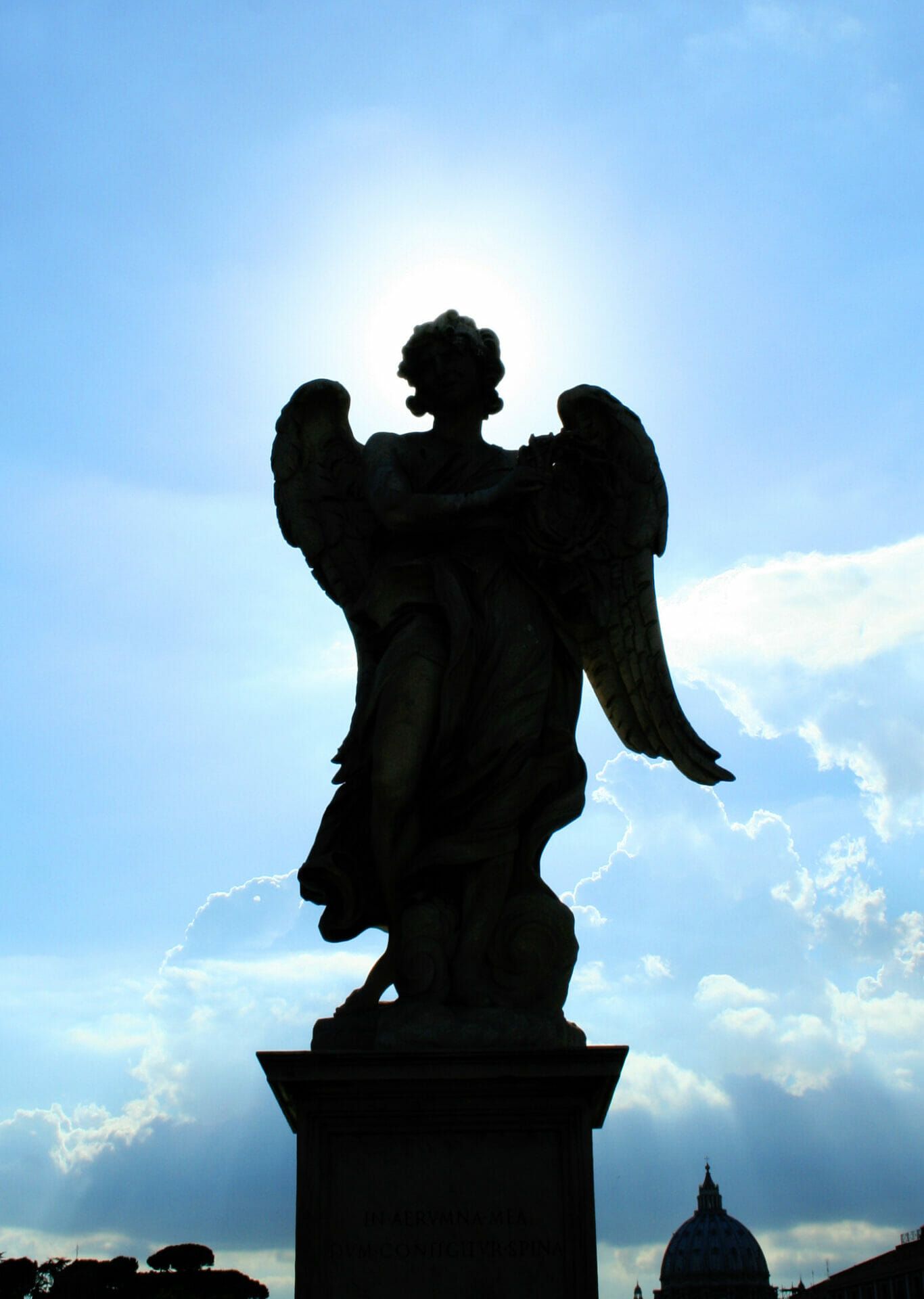 A statue of an angel is silhouetted against a cloudy sky