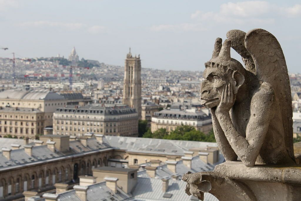 A gargoyle sits on top of a building overlooking a city