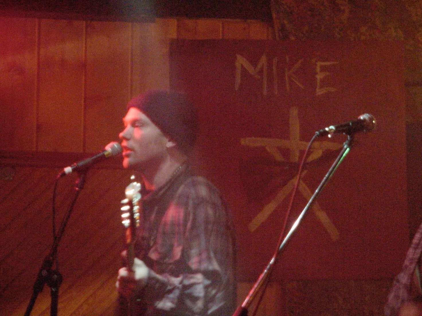 A man singing into a microphone in front of a wall that says mike