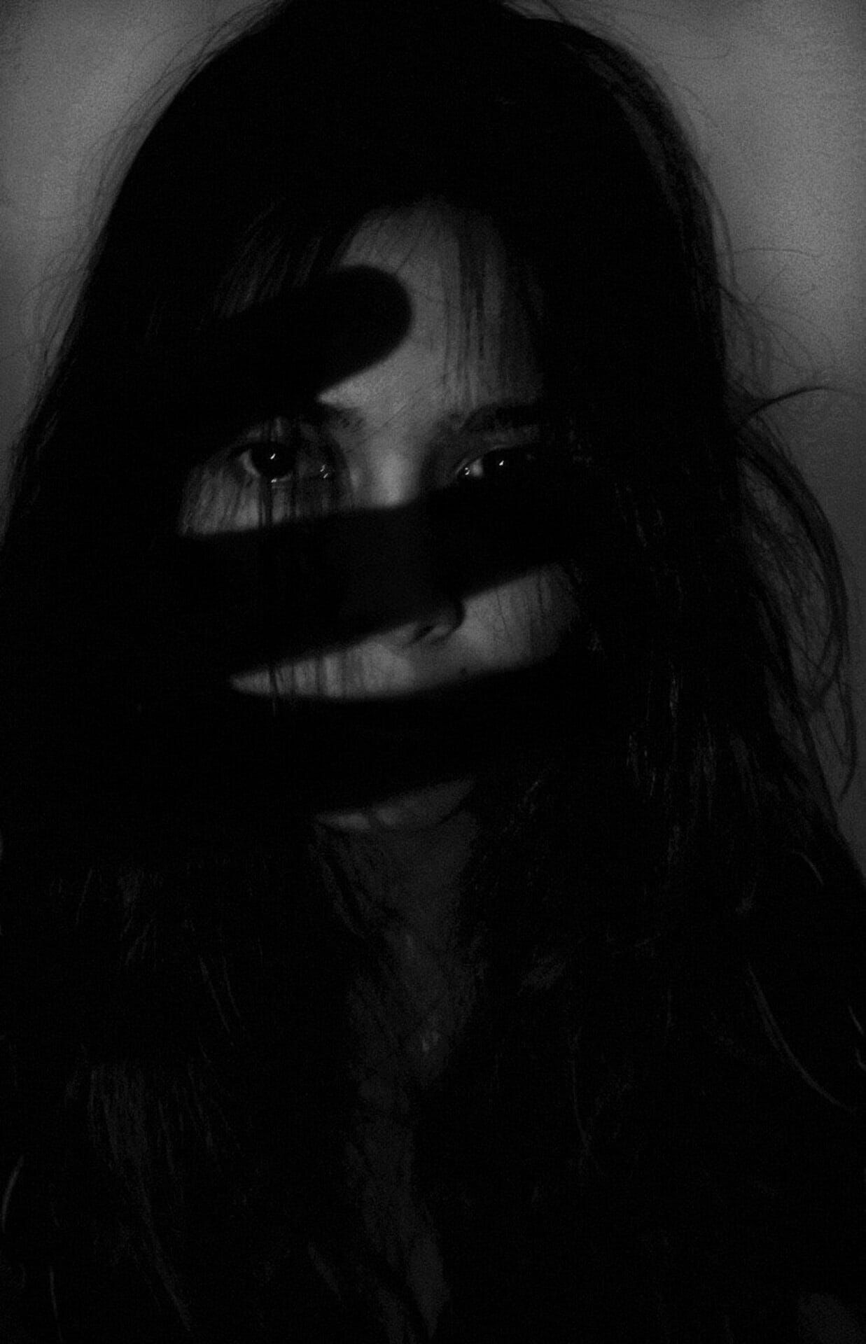 A black and white photo of a woman covering her face with a black cloth.