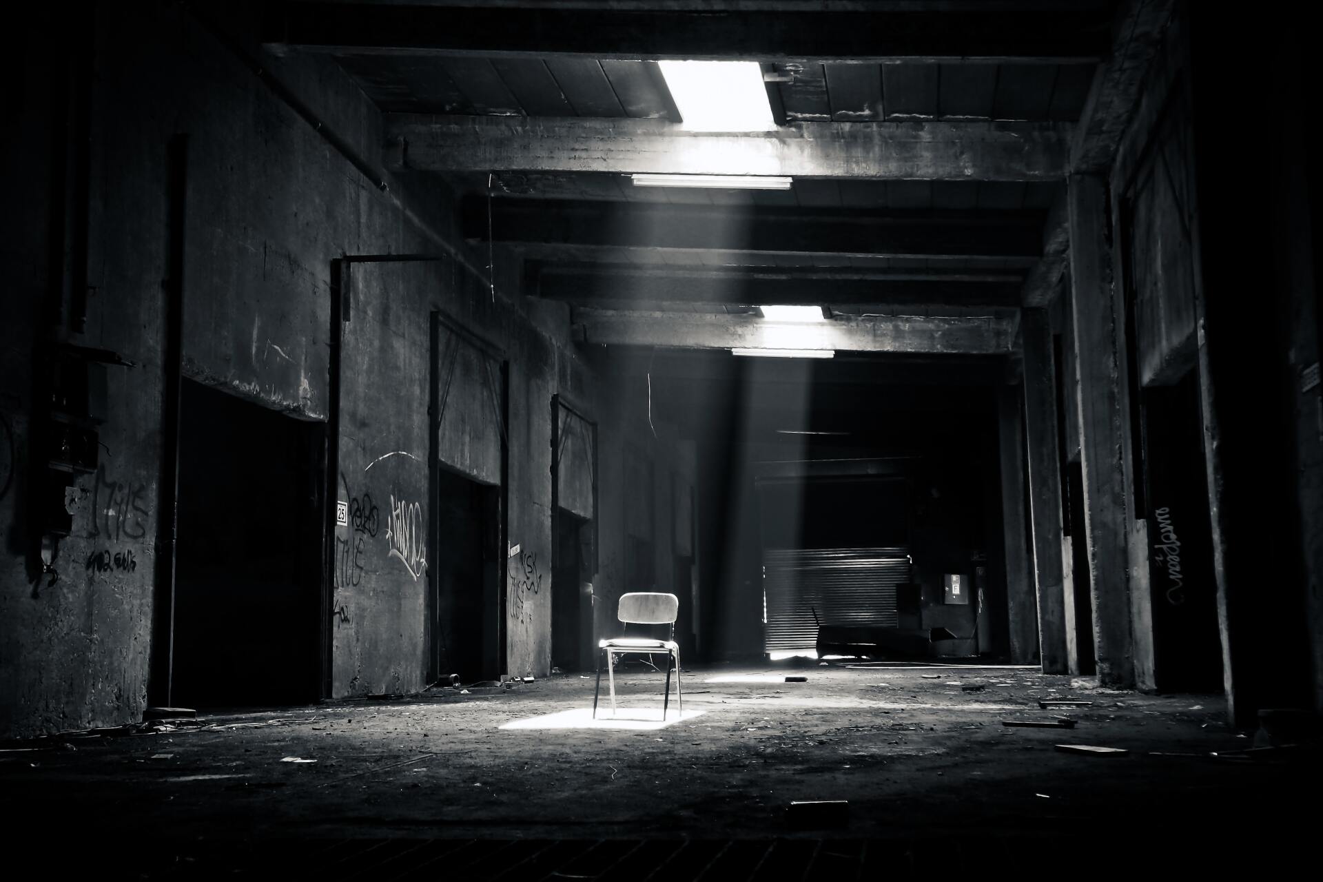 A black and white photo of a dark hallway with a chair in the middle.