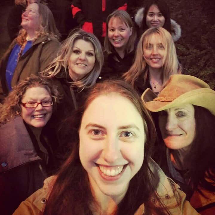 Group of smiling women taking a selfie outdoors at night; one wears a cowboy hat.