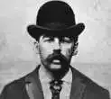 A black and white photo of a man with a beard wearing a bowler hat and tie.