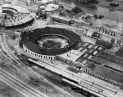 A black and white photo of a train track with a stadium in the background.