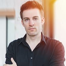 A man in a black shirt is standing with his arms crossed and looking at the camera.