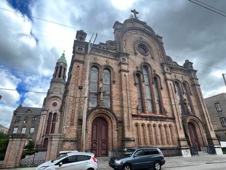 Two cars are parked in front of a large brick church.