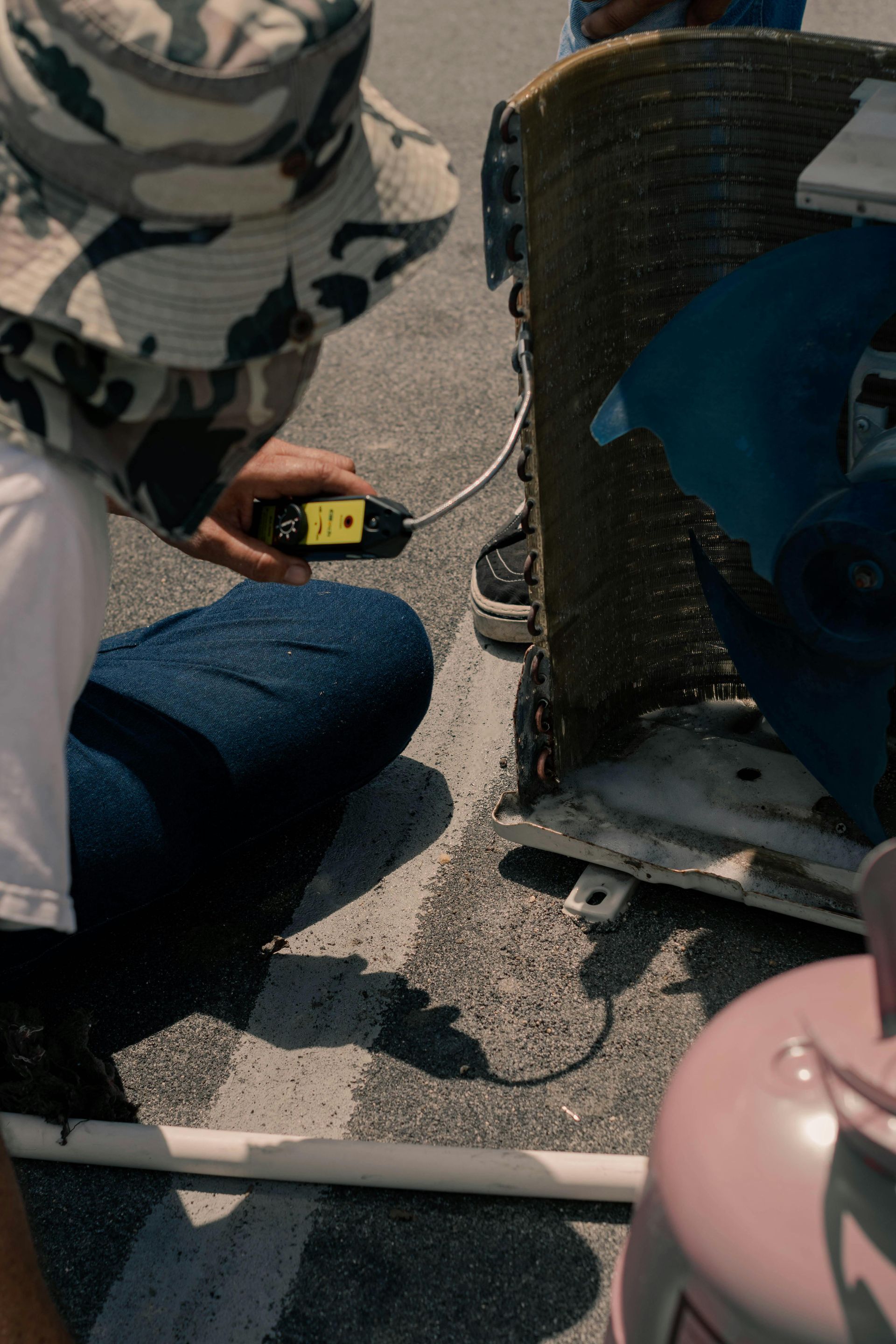 A man in a hat is kneeling down next to an air conditioner.