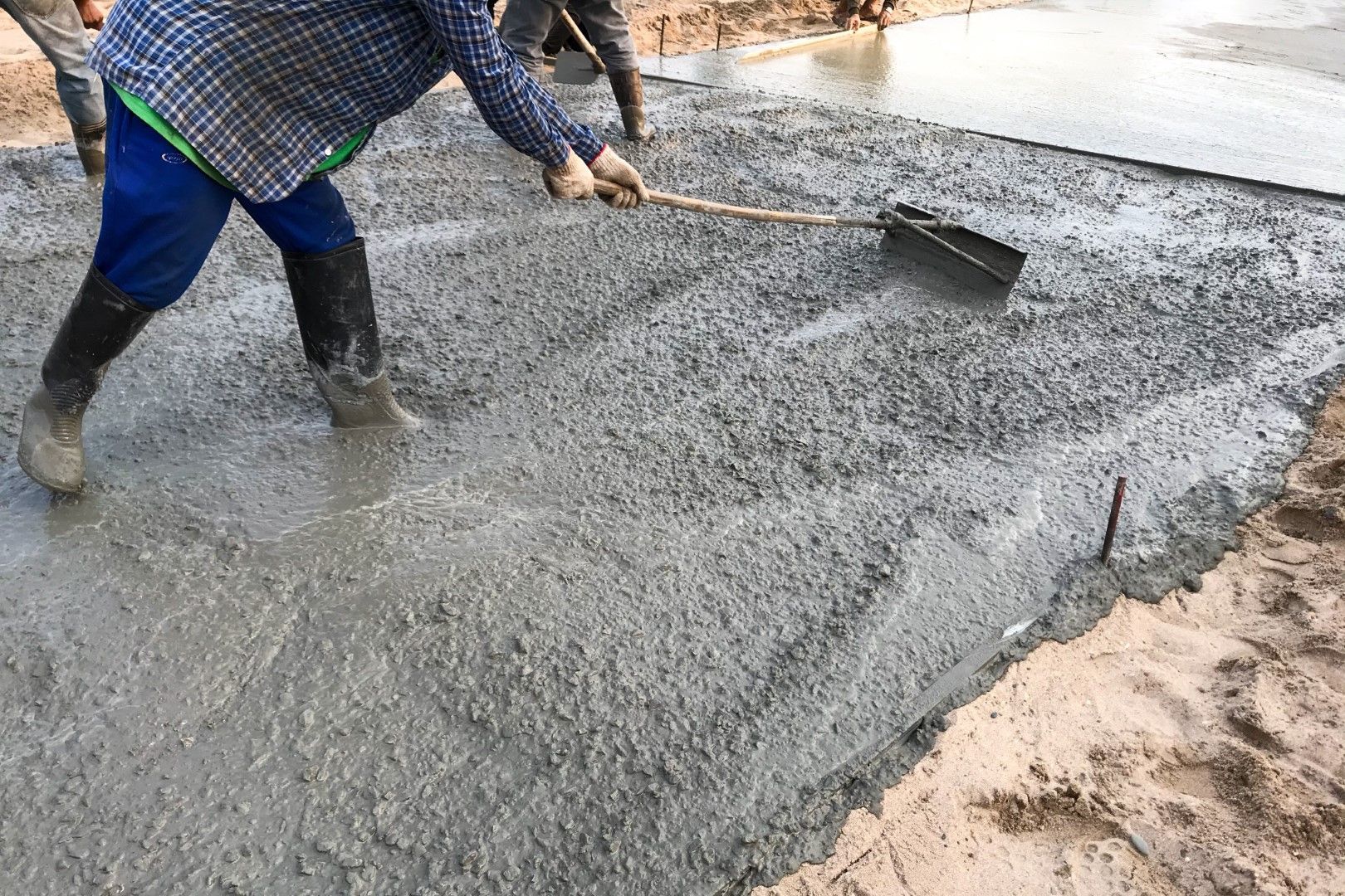 Worker using a rake to level wet concrete on a construction site.